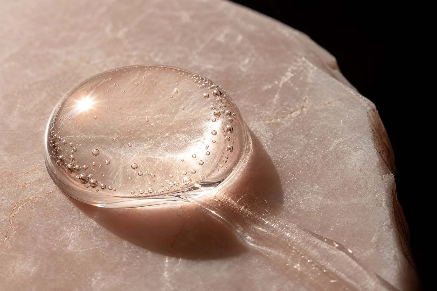 Makroaufnahme eines klaren Serumtropfens auf rosé Stein